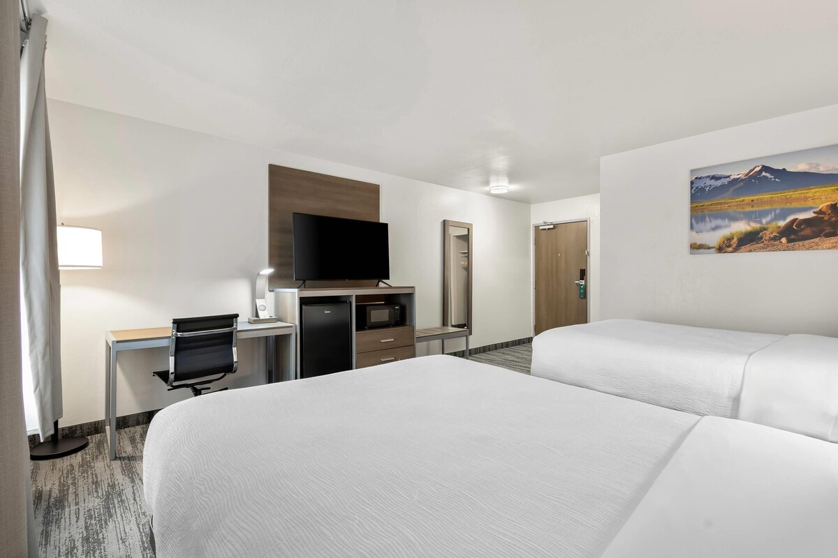 A hotel room with two beds, a desk with a computer, a TV, and a mirror.