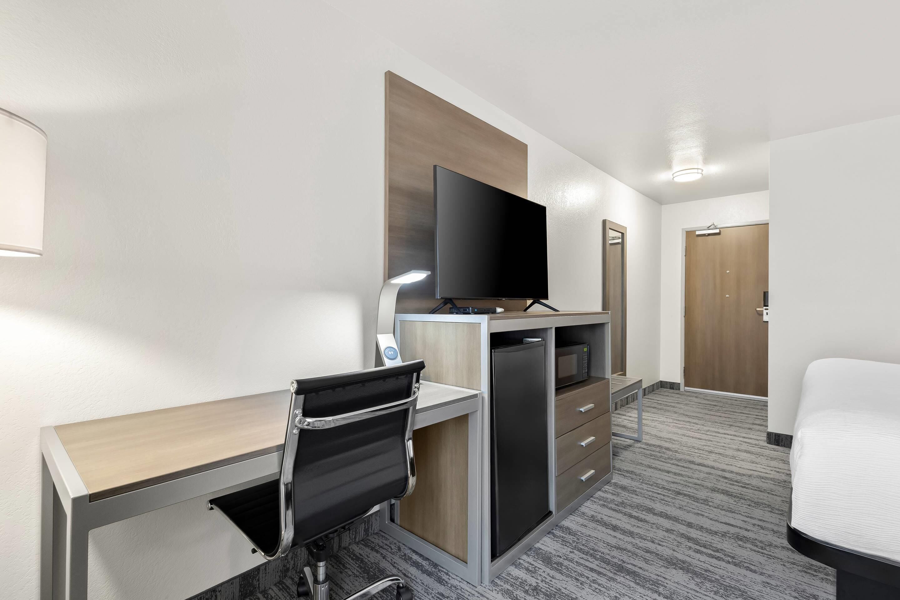 A hotel room with a desk, chair, television, and a bed.