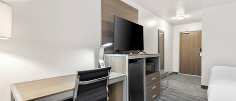 A hotel room with a desk, chair, television, and a bed.