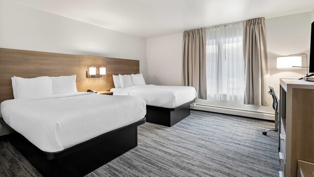 Habitación de hotel con dos camas, cabecera de madera, un escritorio con lámpara y un ventanal con cortinas.