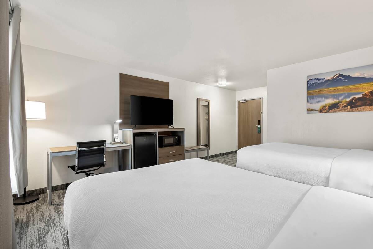 A hotel room with two beds, a desk with a computer, a TV, and a microwave.