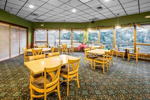 A dining area with multiple tables and chairs, large windows with curtains, and a patterned carpet.