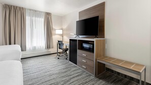 Habitación de hotel con cama, escritorio con computadora, televisor de pantalla plana, microondas y una mesita.