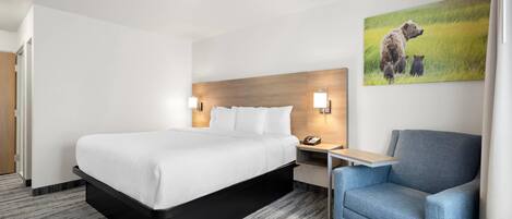 Una habitación de hotel con una cama, una mesita de noche, una lámpara y un sillón azul.