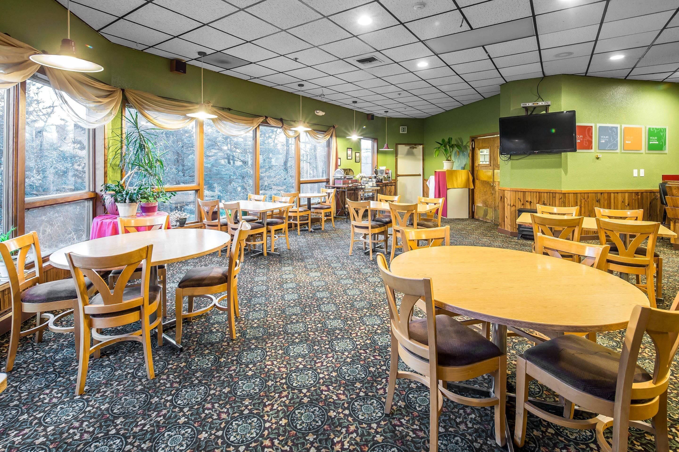 A dining area with round tables and chairs, a patterned carpet, and a television mounted on the wall.