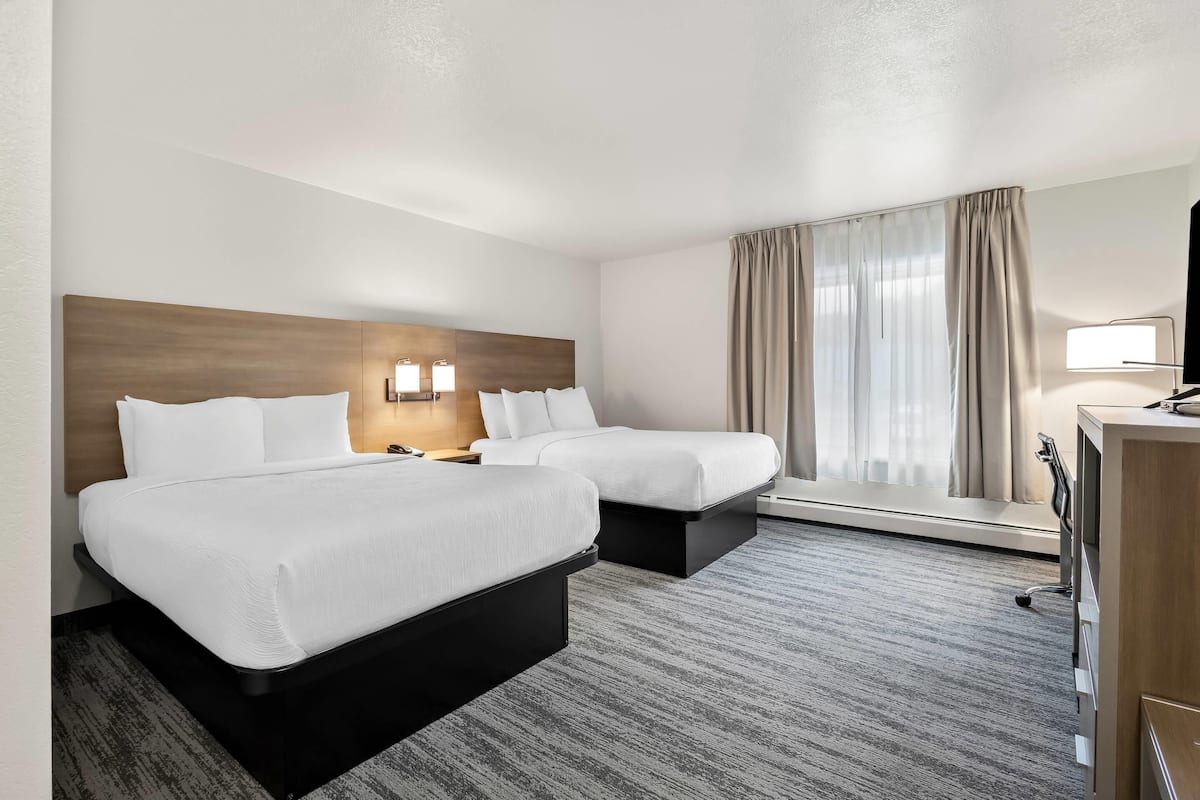 Hotellihuone, jossa on kaksi sänkyä, työpöytä, lamppu ja ikkuna, jossa on verhot.