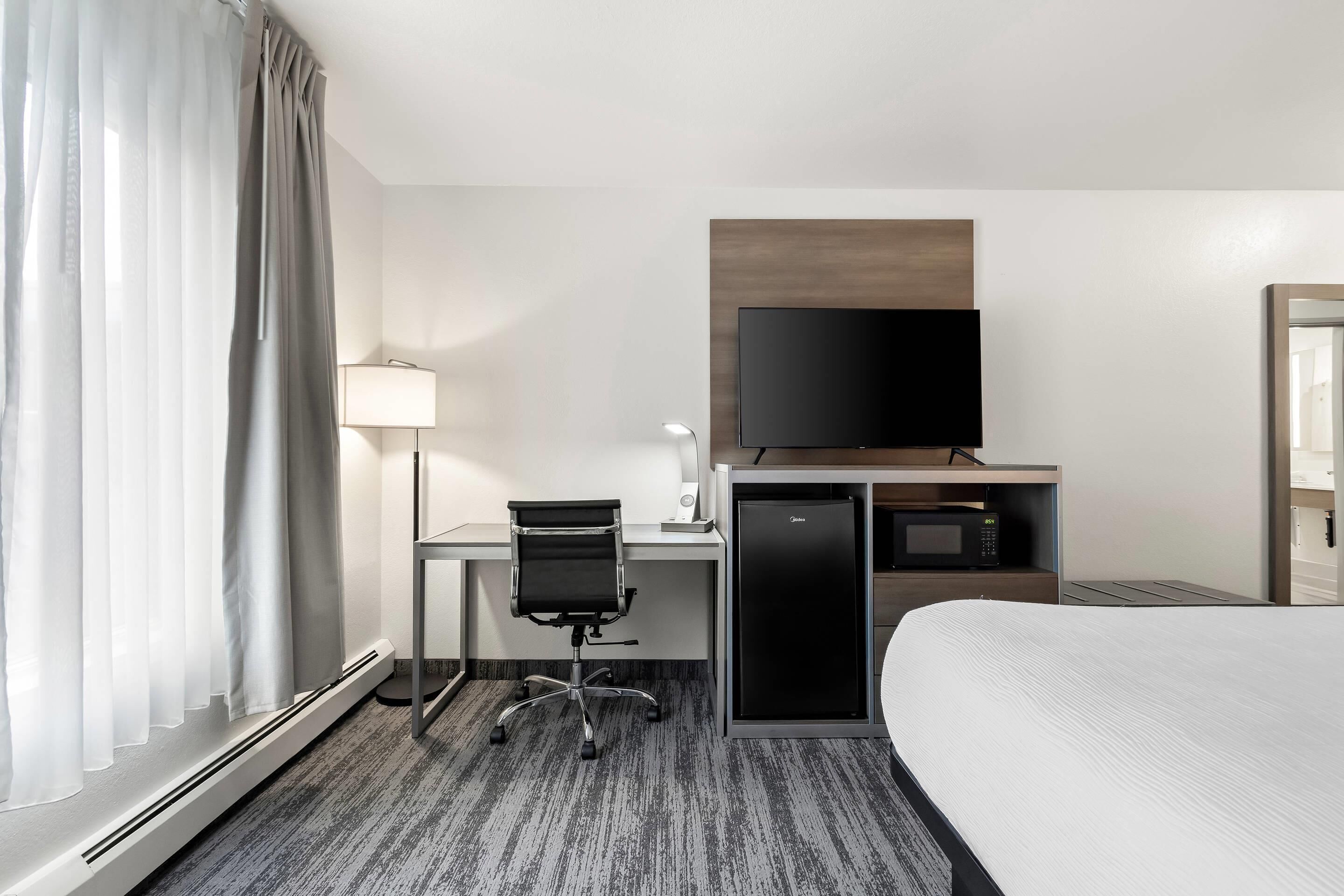A hotel room with a bed, a desk with a chair, a television, a microwave, and a lamp.