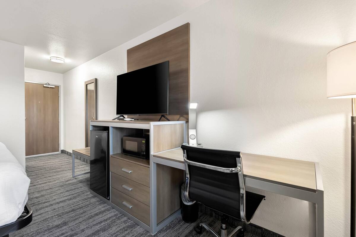 A hotel room with a bed, a desk with a chair, a television, a microwave, and a wardrobe.
