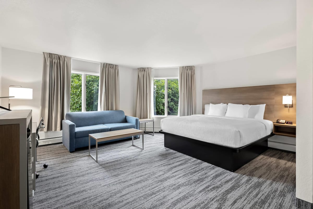 A hotel room with a bed, a blue sofa, a small table, and a desk with a lamp.