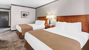 Habitación de hotel con dos camas, una mesita de noche con lámpara, un cuadro enmarcado en la pared y una puerta que da a otra habitación.