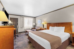 A hotel room with a large bed, a desk, a chair, a lamp, and a window with curtains.