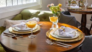 A dining table set with plates, glasses, and cutlery, a vase with flowers, and a window with a stained glass design. - Arsenic and Old Lace B&B (Eureka Springs)