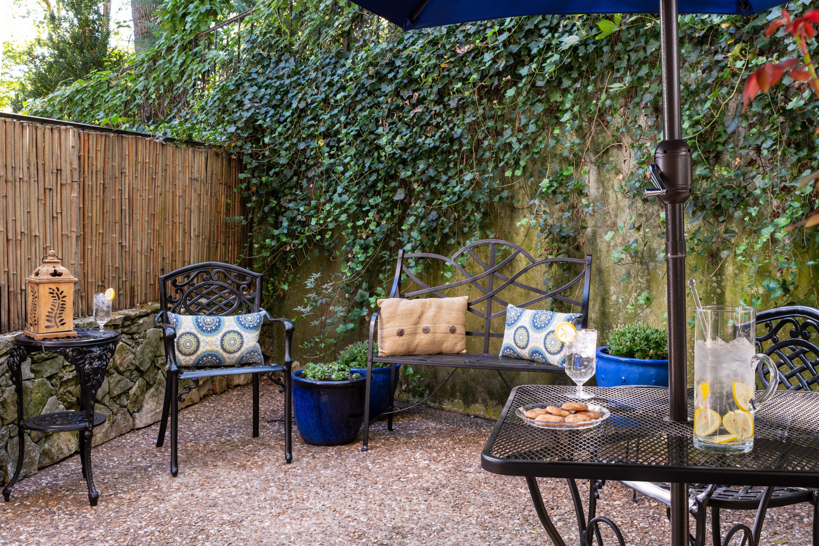 Un patio esterno con un tavolo apparecchiato per due, con una caraffa di limonata, un piatto di biscotti e una lanterna.