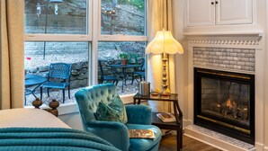 A bedroom with a large bed, a blue armchair, a fireplace, and a view of an outdoor patio with a table and chairs. - Arsenic and Old Lace B&B (Eureka Springs)