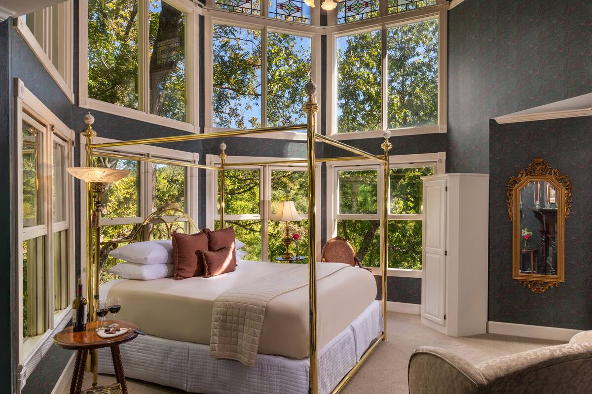 A bedroom with a four-poster bed, large windows, and a chandelier.