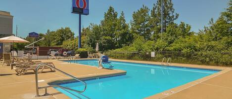 A swimming pool with lounge chairs and a motel sign in the background.