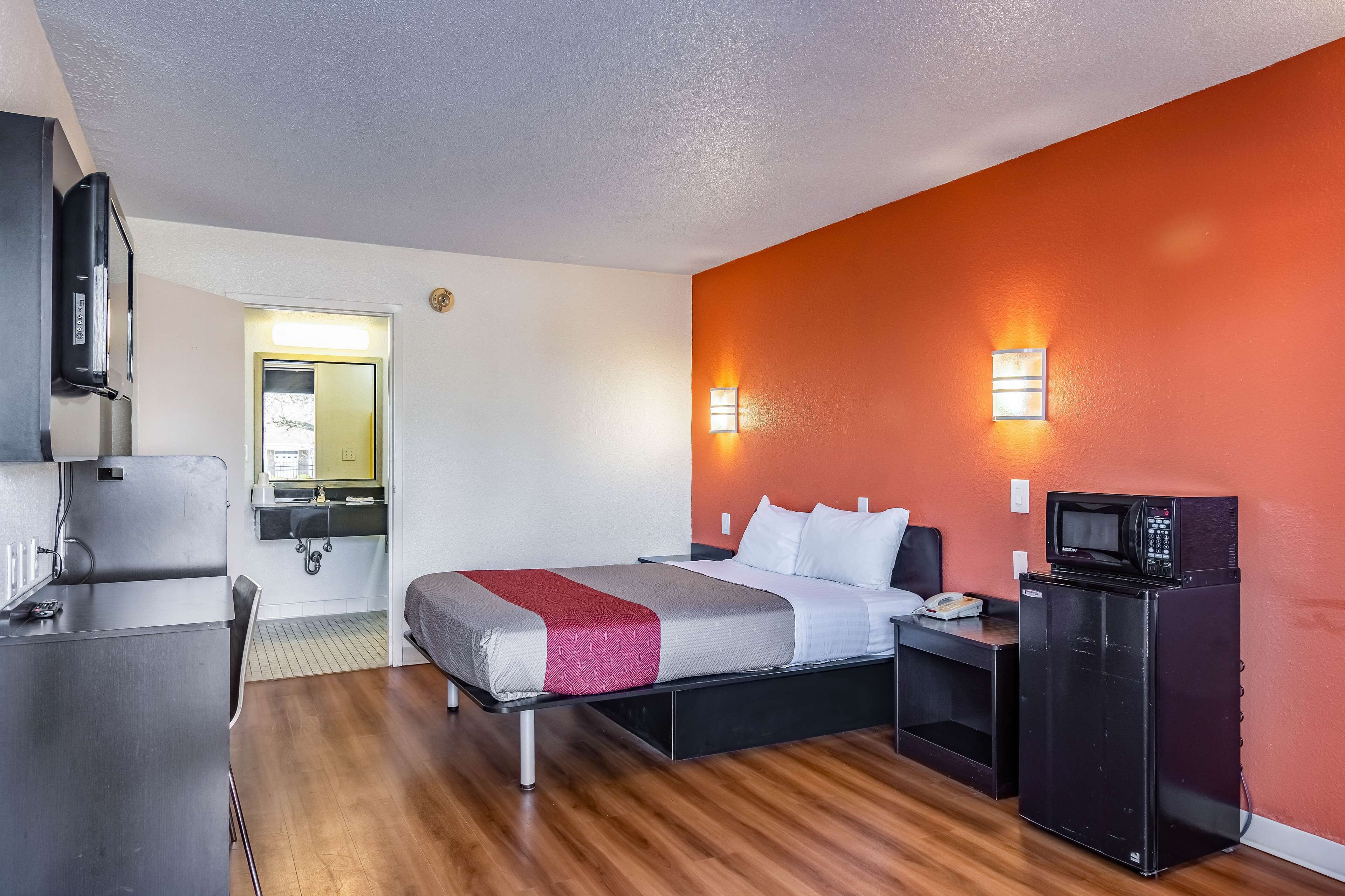 A compact hotel room with a bed, a desk, a microwave, and a small kitchenette.