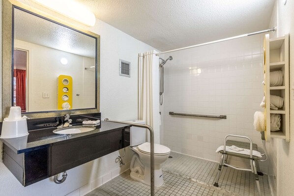 Un baño con lavamanos negro, inodoro blanco y zona de ducha con barra de apoyo.