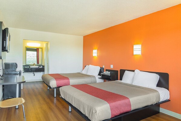 Une chambre d’hôtel avec deux lits, un bureau, une chaise et une salle de bain visible à travers une porte ouverte.