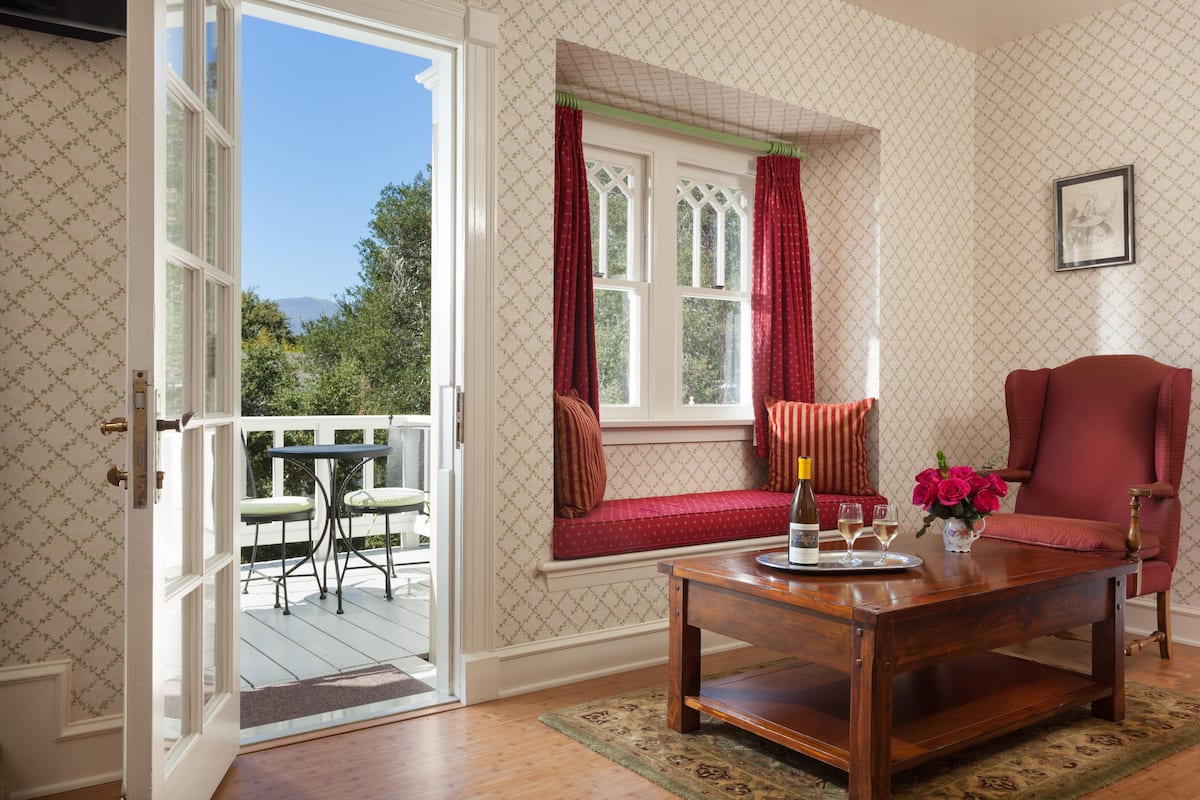 A room with a wooden coffee table, a red chair, a bench with red cushions, and a window with red curtains.
