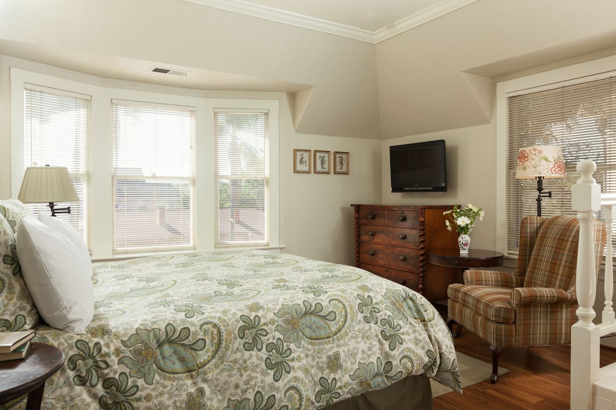 A bedroom with a large bed, a dresser, a television, and a chair.