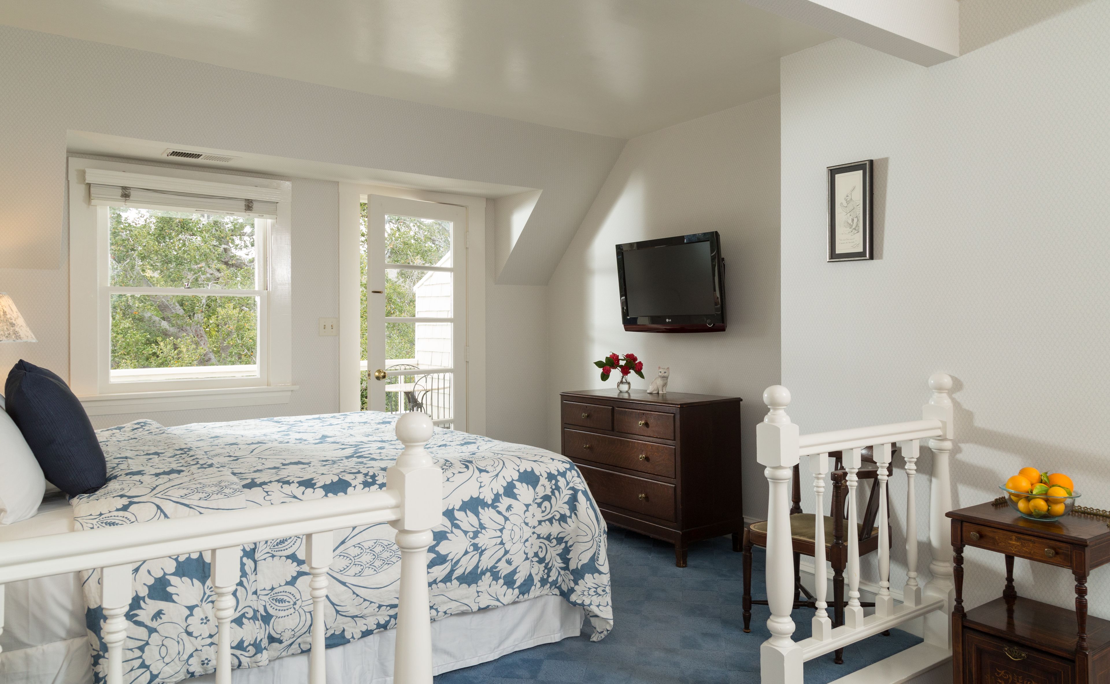 A bedroom with a bed, dresser, TV, and a small table with fruit.