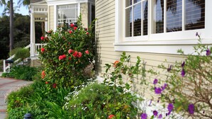Una casa con ventanal saliente, porche y jardín con diversas plantas y flores.