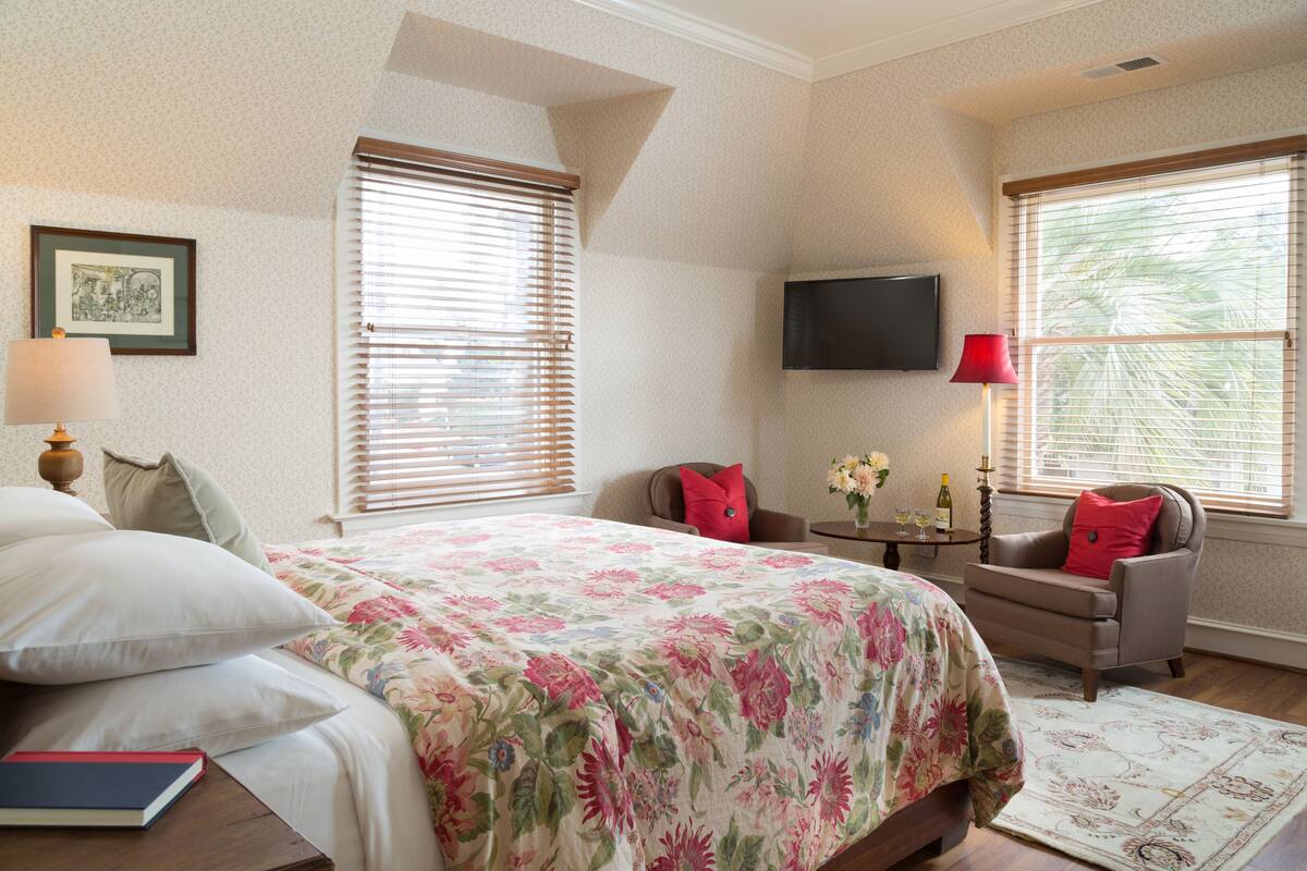 A bedroom with a bed, a chair, a TV, and a window with blinds.