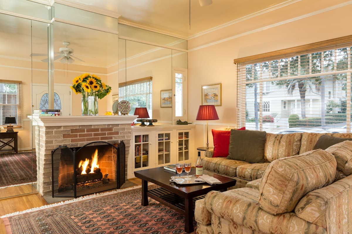 A living room with a fireplace, a sofa, a coffee table, and a large mirror reflecting the room.