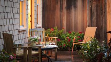A wooden deck with a table and chairs, surrounded by potted plants and flowers.