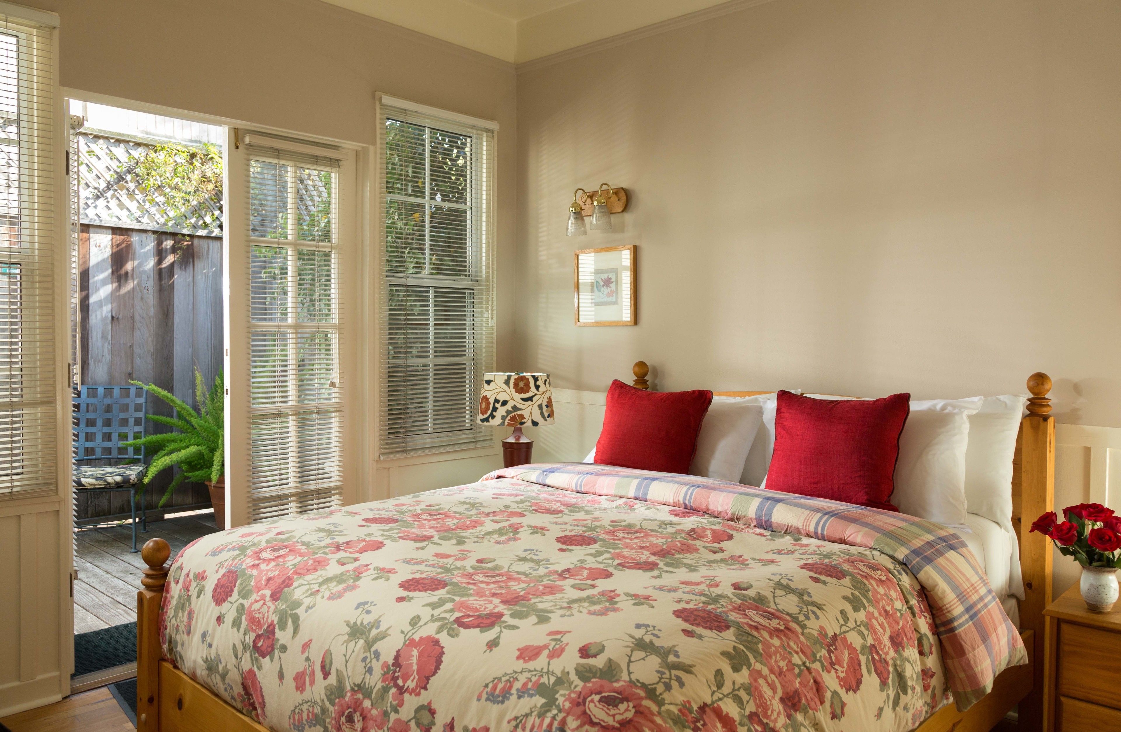 Un dormitorio con colcha estampada de flores, cabecera de madera y mesita de noche con un jarrón de flores.