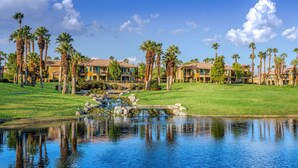 Een resort met meerdere gebouwen, een vijver en palmbomen.