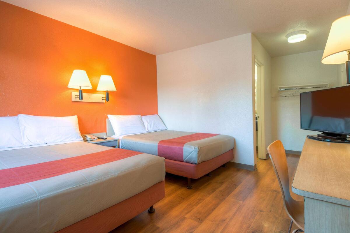 A hotel room with two beds, a desk with a chair, a television, and two wall-mounted lamps.