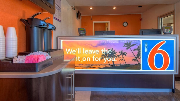 A hotel reception desk with a digital display, a coffee station, and a view of the lobby. - Motel 6 San Ysidro, CA - San Diego - Border (San Ysidro)