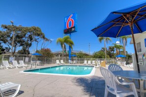 A motel with a swimming pool, lounge chairs, and umbrellas.