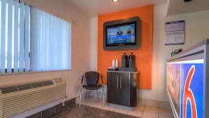 A hotel room with a large window, a television mounted on the wall, a cabinet with toiletries, and a sign indicating room prices. - Motel 6 San Ysidro, CA - San Diego - Border (San Ysidro)
