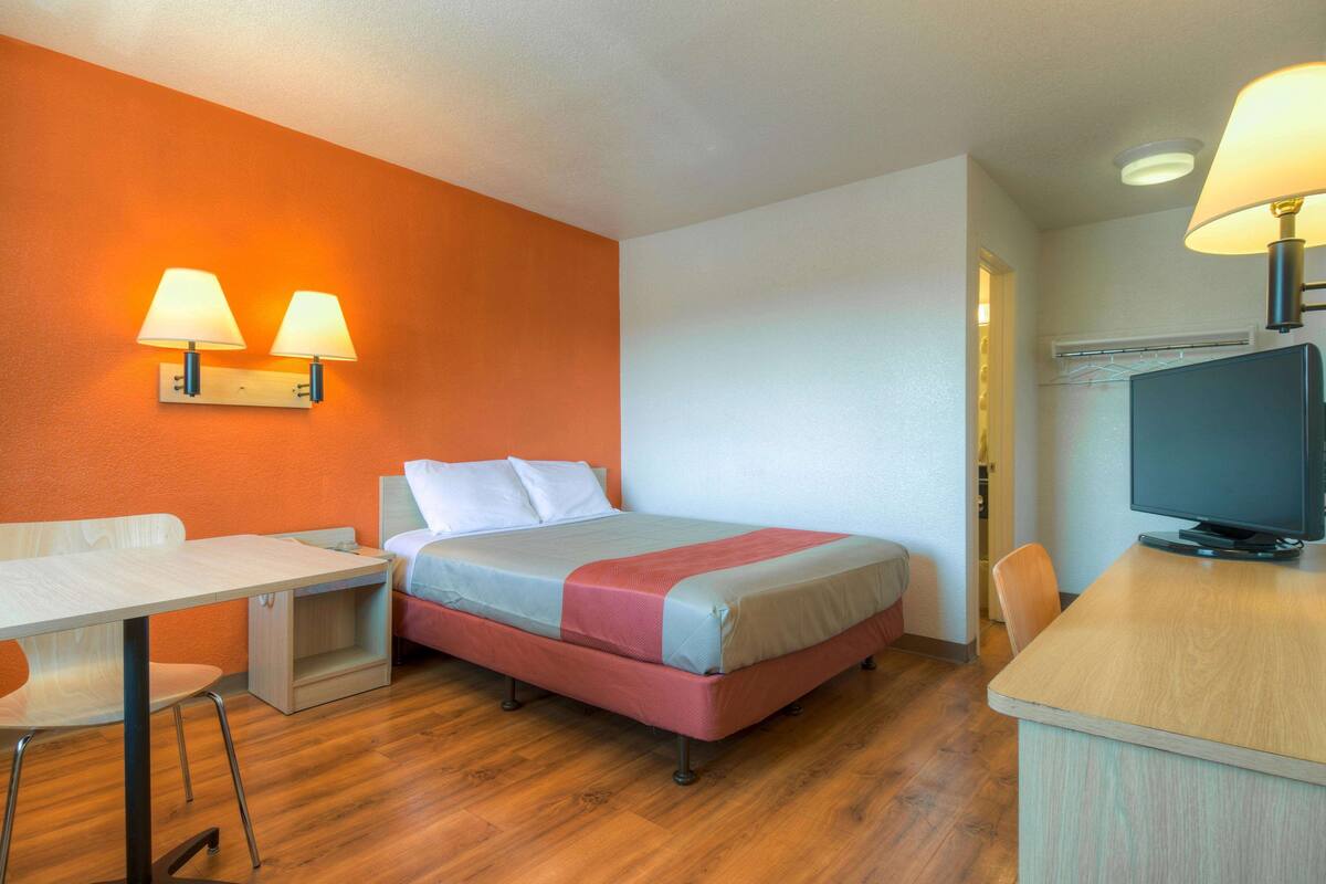 A hotel room with a bed, a desk, a chair, and a television.
