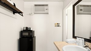 A bathroom with a sink, mirror, towel rack, and a microwave on a black cabinet. - Vagabond Inn Los Angeles at USC (Los Angeles)