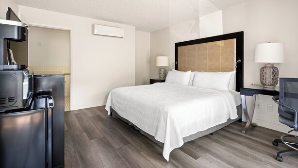 A hotel room with a bed, a desk, a chair, a coffee machine, and a lamp. - Vagabond Inn Los Angeles at USC (Los Angeles)