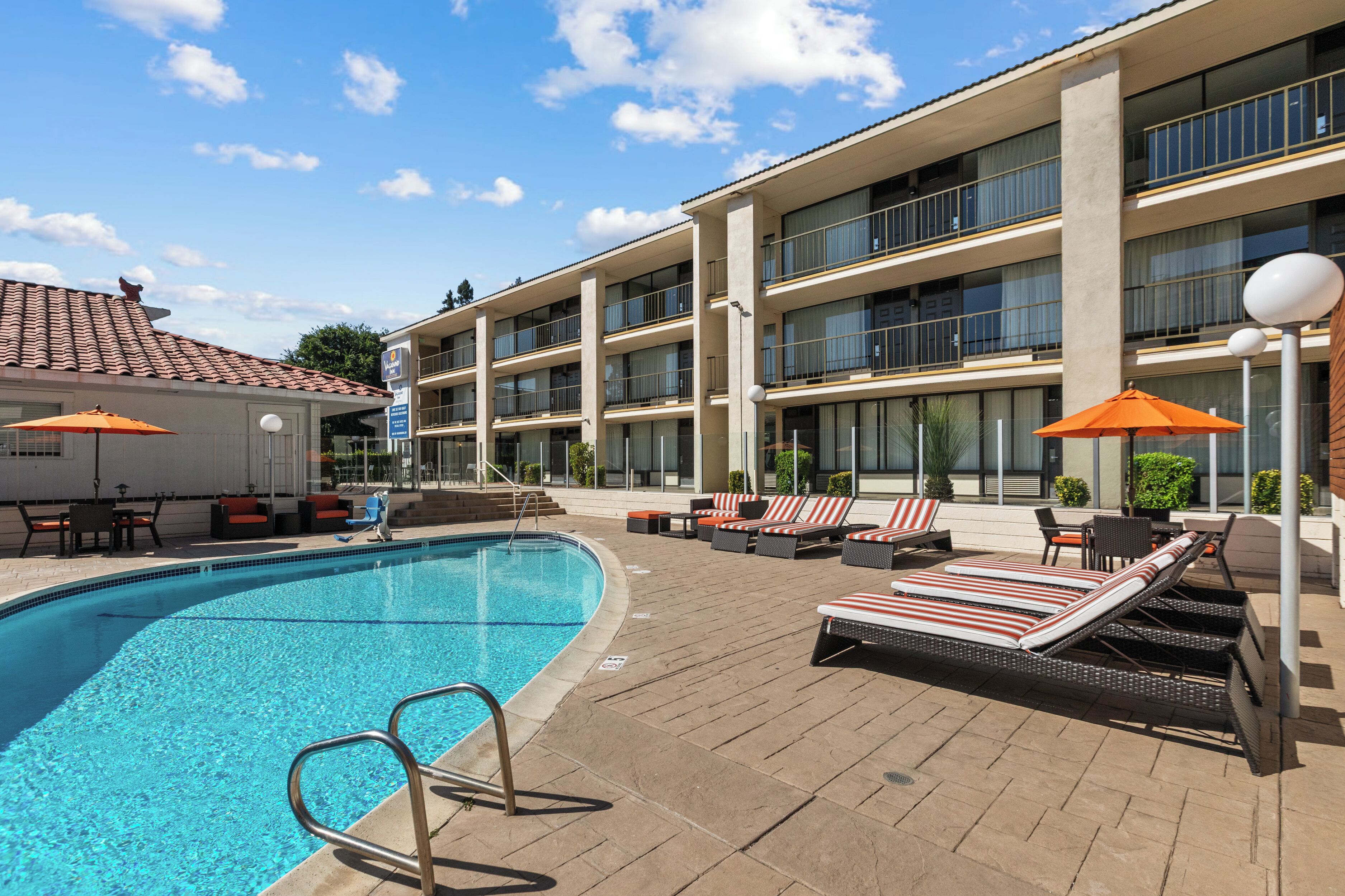 A hotel pool area with a clear blue pool, sun loungers, and umbrellas.