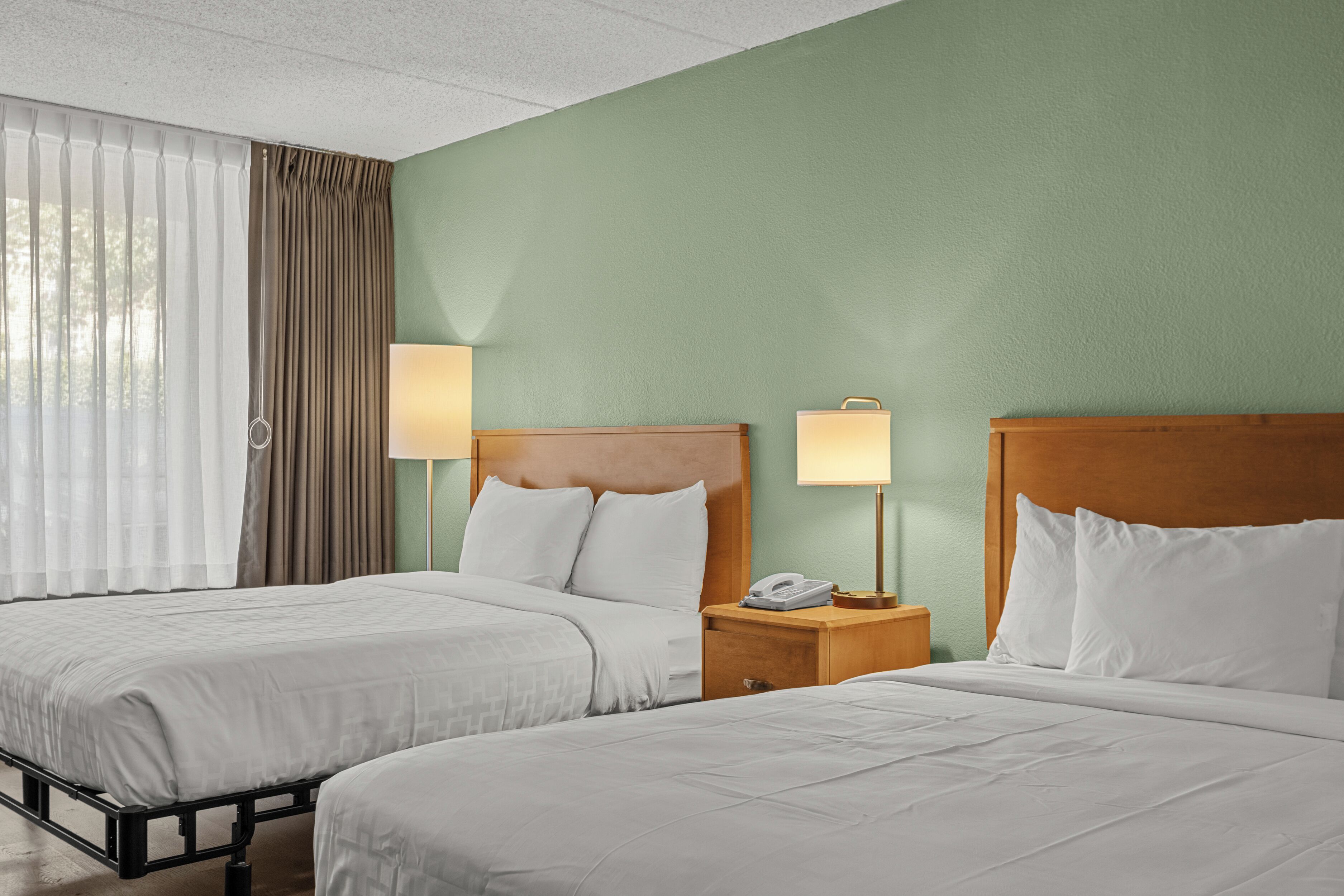Een hotelkamer met twee bedden, een houten hoofdeinde, een nachtkastje met een lamp en een telefoon.