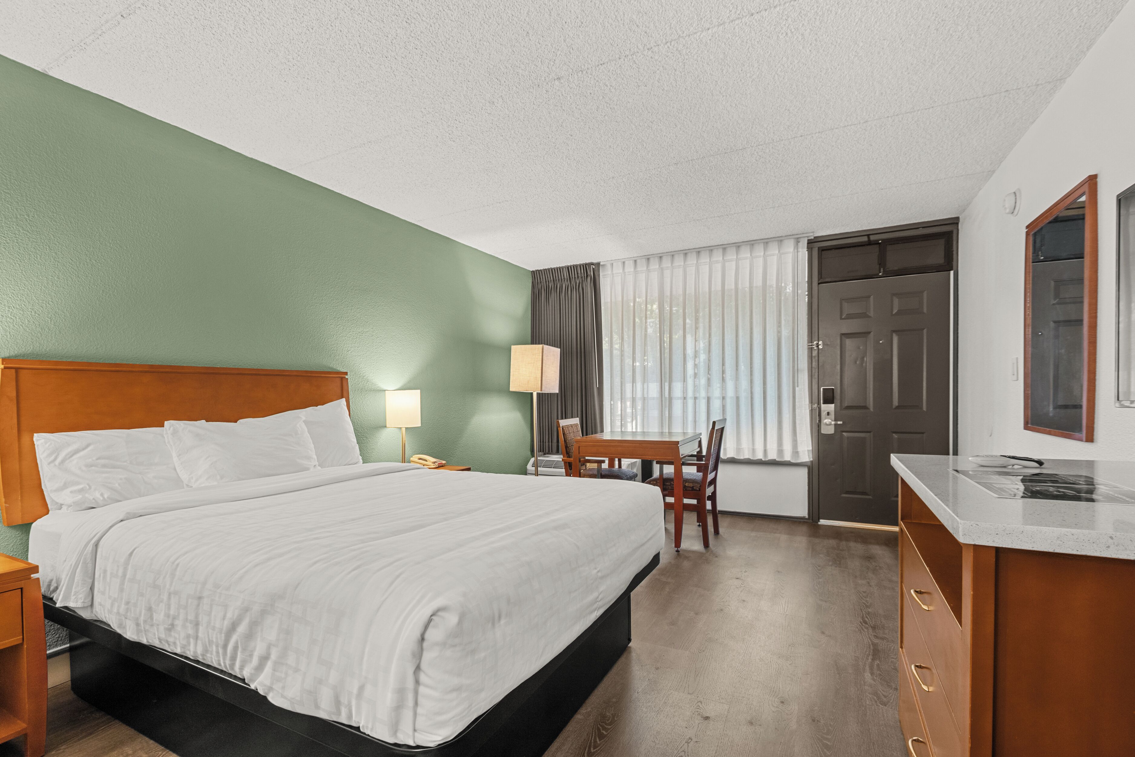 A hotel room with a large bed, a desk with a chair, a dresser, and a door.