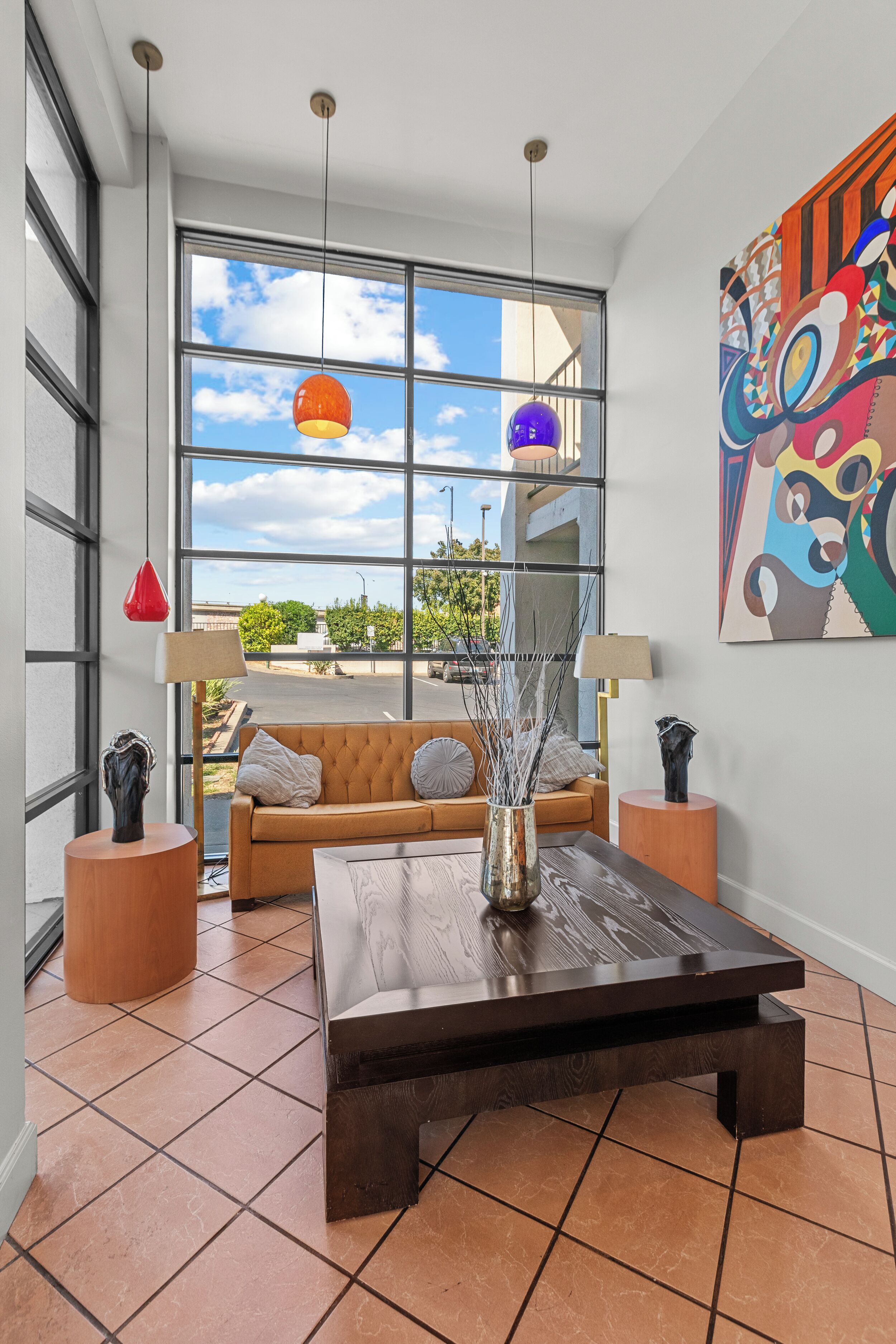 A modern living room with a large window, a brown sofa, a coffee table, and two lamps.