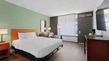 A hotel room with a bed, a desk, a chair, a TV, and a door.