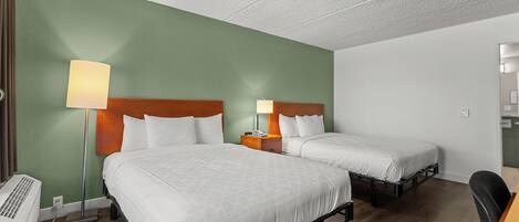 A hotel room with two beds, a desk, a chair, a lamp, and a heater.