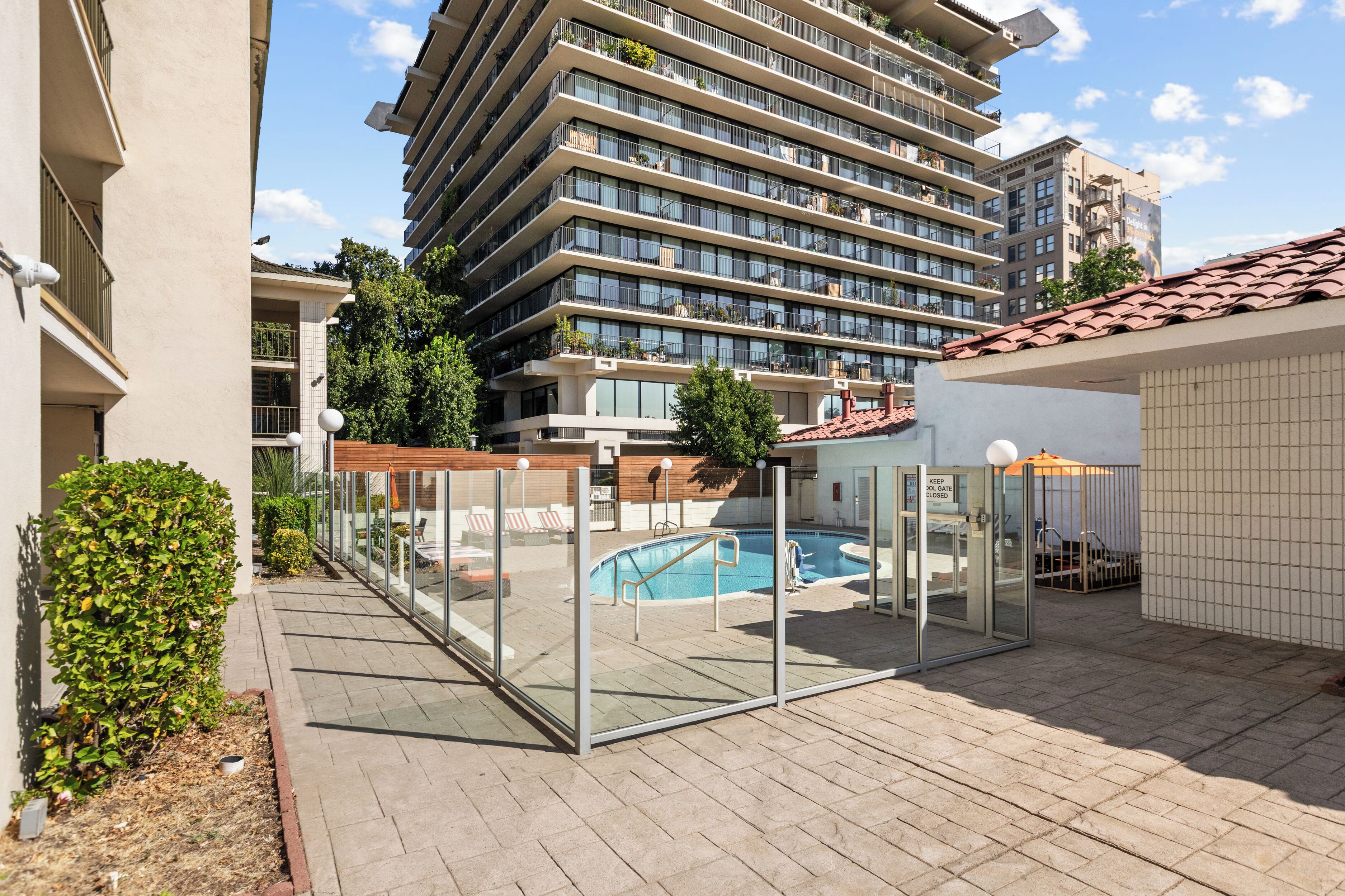 A modern building with multiple balconies, a swimming pool, and a gated entrance.