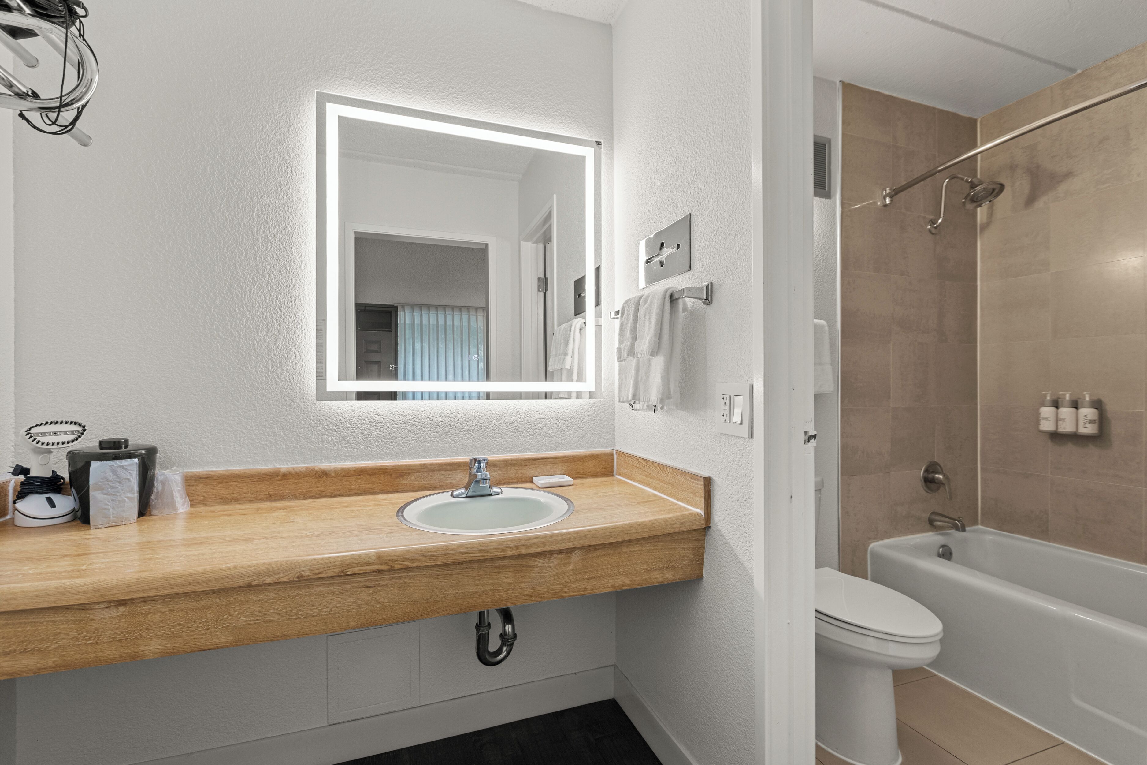 A modern bathroom with a wooden vanity, a white sink, a mirror with LED lighting, a toilet, and a bathtub.