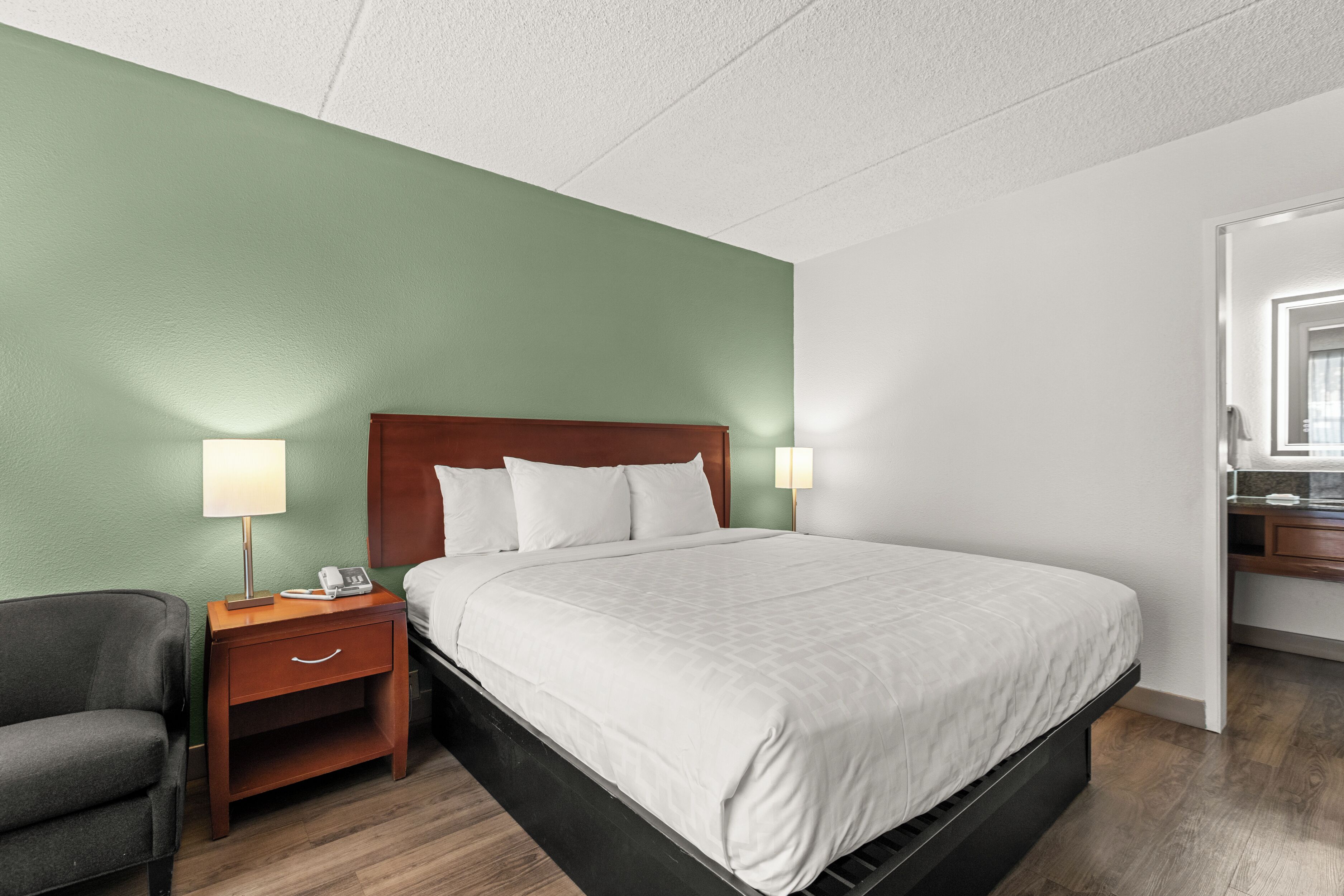 A hotel room with a bed, bedside table, lamp, and a chair.