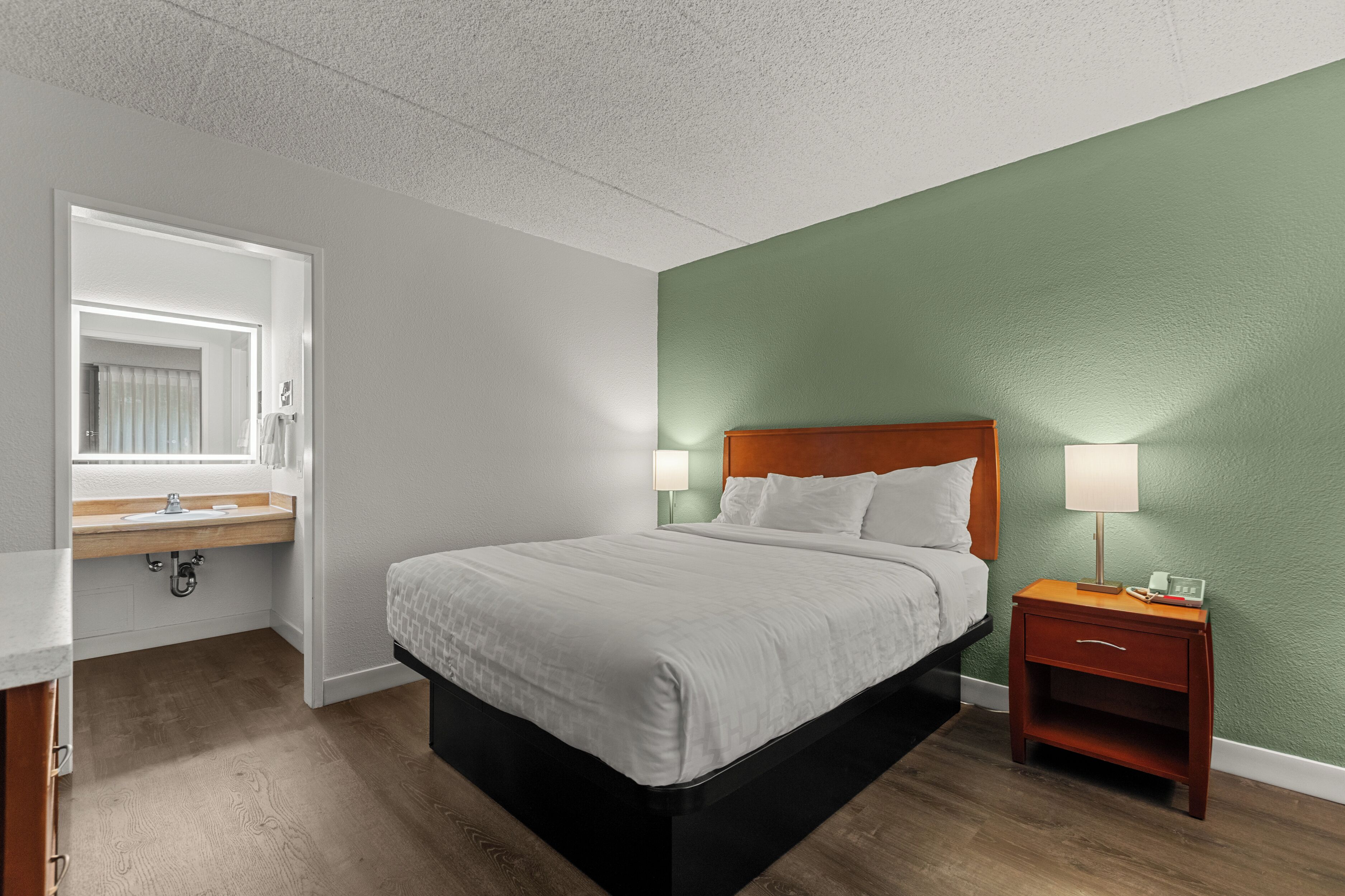 A hotel room with a bed, nightstand, and a bathroom with a sink and mirror.