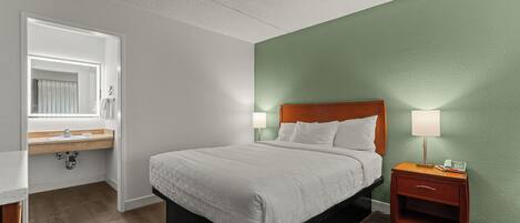 A hotel room with a bed, nightstand, and a bathroom with a sink and mirror.